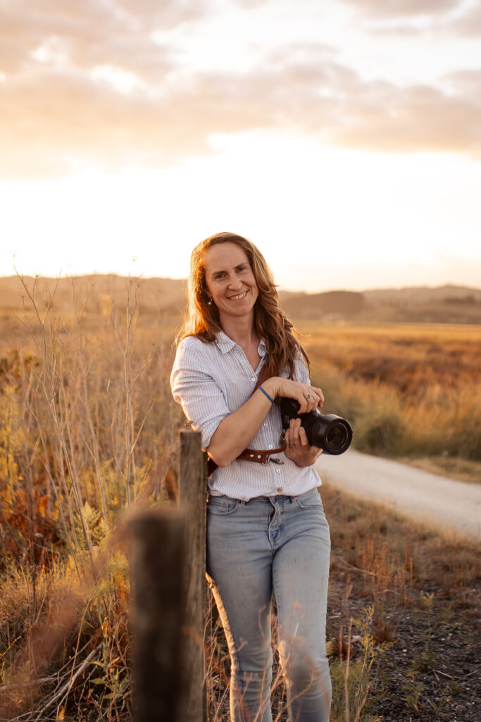 Hawke’s Bay motherhood photographer Katherine smiling and holding her camera at sunset, showing her relaxed and friendly approach.