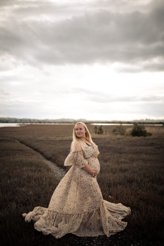 Pregnant woman standing at Pandora Estuary in Hawke’s Bay at sunset, wearing a flowing dress, natural maternity photography.

Image Title: