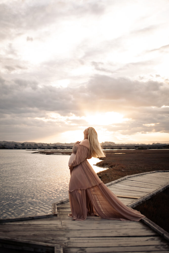Maternity photography at Pandora Estuary, Hawke’s Bay. Pregnant woman swishing her hair in the golden sunset, wearing a flowing dress.