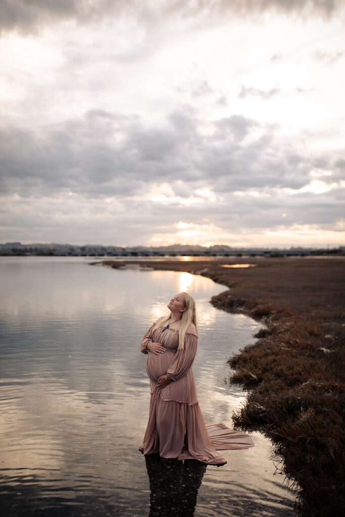 Pregnant woman standing in shallow water at Pandora Estuary, Hawke’s Bay during sunset maternity photography.