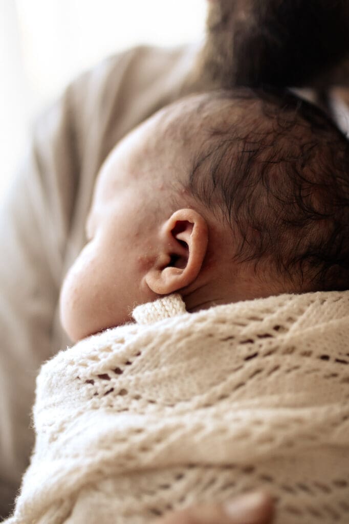 Newborn Baby's ears sleeping in dads arms during an newborn baby in home photoshoot in Hawkes Bay NZ